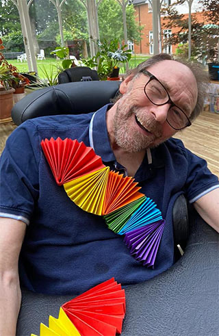 A King’s Lodge resident smiling with colourful paper crafts in the conservatory